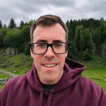 Chris Naylor, smiling in a maroon hoodie with a forested Norwegian hillside behind